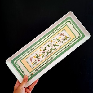 Pode incluir: Uma bandeja de servir retangular branca com uma ilustração botânica central de flores de jasmim amarelo, folhas verdes e pequenas borboletas. O design inclui o texto Jasminum Revolutum Yellow Jasmine e uma borda de folhas verdes.