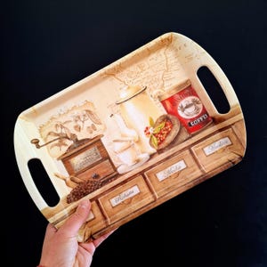 Könnte beinhalten: Ein rechteckiges Serviertablett mit Kaffeemotiv. Das Tablett hat ein Vintage-Design mit Bildern von Kaffeebohnen, einer Kaffeemühle, einer Teekanne und einer Kaffeedose. Das Tablett hat zwei Griffe und die Wörter "Robusta", "Mocha" und "Arabica" sind sichtbar.