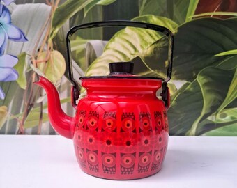 May include: A bright red enamel teapot featuring a repeating geometric pattern in dark red and orange. The teapot has a black lid knob, a curved spout, and a black metal handle that arches over the top. The body is round with a flat base.