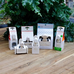 May include: Five white paper packaging boxes with Martha Stewart brand paper punches. The punches are for creating decorative edges on paper. The boxes are on a wooden surface.