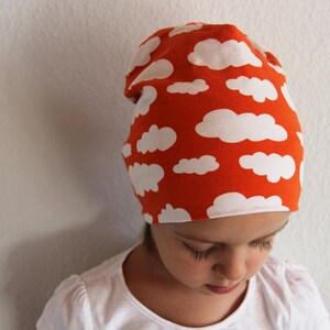 Puede incluir: Un ni&ntilde;o o ni&ntilde;a lleva una boina roja con un patr&oacute;n de nubes blancas. La boina est&aacute; hecha de un tejido suave y el&aacute;stico.