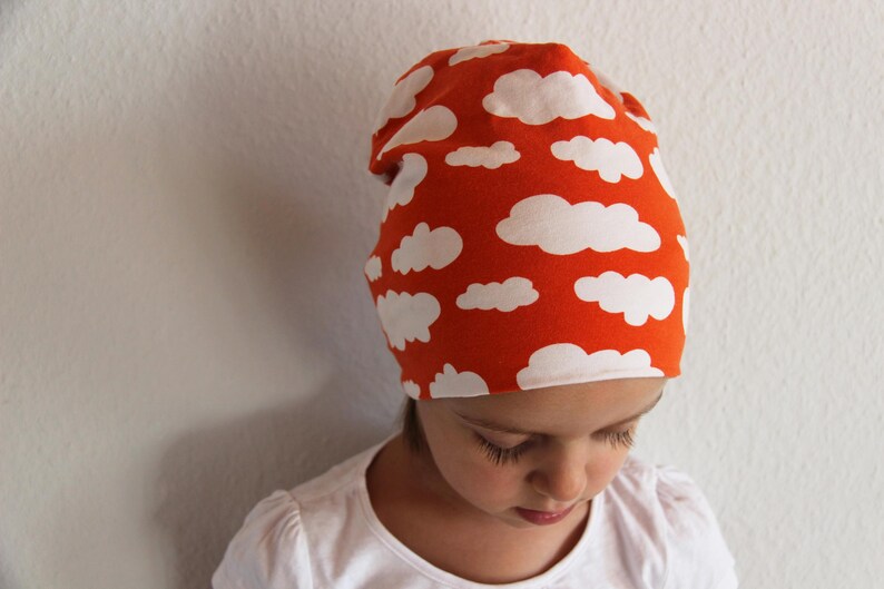 Puede incluir: Un ni&ntilde;o o ni&ntilde;a lleva una boina roja con un patr&oacute;n de nubes blancas. La boina est&aacute; hecha de un tejido suave y el&aacute;stico.