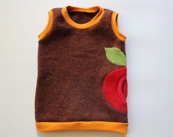 Op de afbeelding: Een bruin, mouwloos shirt met een rood en groen appelontwerp. Het shirt heeft een gele bies rond de hals en armsgaten.