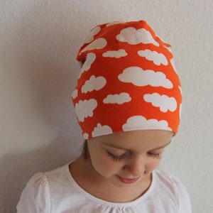 Puede incluir: Un ni&ntilde;o o ni&ntilde;a lleva una boina de color naranja brillante con un patr&oacute;n de nubes blancas. La boina est&aacute; hecha de un tejido suave y el&aacute;stico.