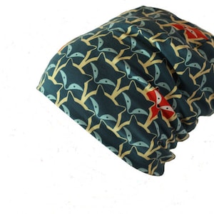 Puede incluir: Un gorro azul verdoso con un patrón repetido de caras de zorro estilizadas en amarillo y rojo.