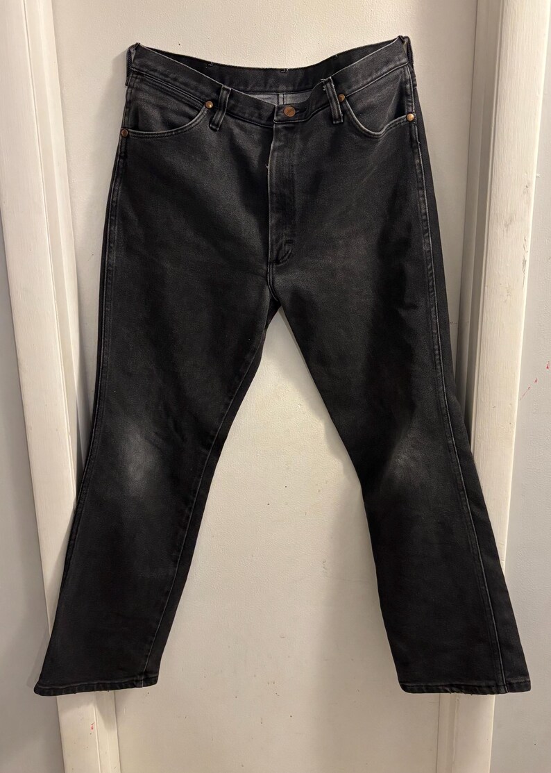 May include: Black denim jeans with a classic five-pocket design. The jeans have a button and zip closure, and a faded appearance. The jeans are a straight-leg style.