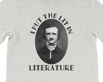 Può includere: Una t-shirt grigia melange con un'immagine in bianco e nero di Edgar Allan Poe e il testo "I put the lit in literature".