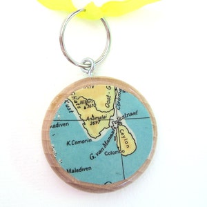 Könnte beinhalten: Ein Holzschlüsselanhänger mit einer Vintage-Karte von Indien und Sri Lanka. Die Karte ist auf blauem Papier mit gelben Akzenten gedruckt. Der Schlüsselanhänger ist an einem silbernen Schlüsselring befestigt.