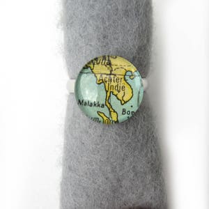 Può includere: Un anello d'argento con un cabochon di vetro che presenta una mappa vintage del sud-est asiatico. La mappa mostra il testo "Achter Indie" e "Malakka".