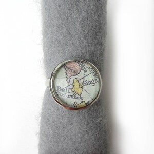 Peut inclure: Une bague en argent avec un cabochon en verre représentant une carte vintage de Bali et des îles environnantes. La carte indique les noms "Bali", "Singa" et "Lombok".