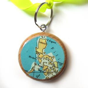 Op de afbeelding: Een houten sleutelhanger met een kaart van de Filippijnen. De kaart is blauw en groen met gele en bruine accenten. De sleutelhanger heeft een zilveren ring.