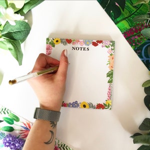 May include: A white notepad with a floral border in shades of pink, red, yellow, and blue. The notepad has the word "NOTES" printed in black at the top.