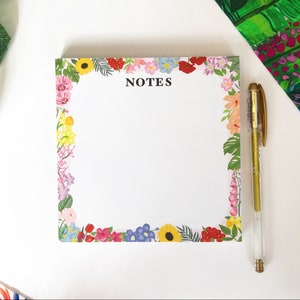 May include: A white notepad with a floral border and the word "NOTES" printed in black at the top. The border features a variety of colorful flowers, including pink, yellow, blue, and red.