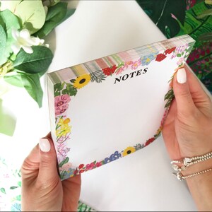 May include: A floral notepad with a white background and a colorful floral border. The notepad has the word "NOTES" printed in black at the top.