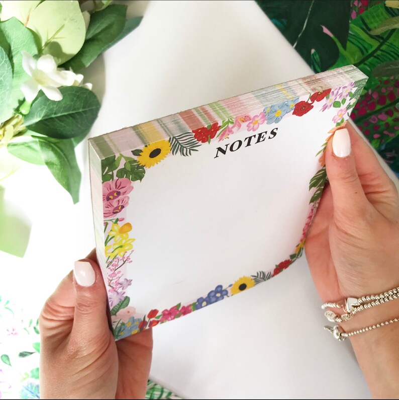 May include: A floral notepad with a white background and a colorful floral border. The notepad has the word "NOTES" printed in black at the top.