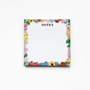 May include: A white notepad with a floral border. The border features a variety of colorful flowers, including pink, red, yellow, blue, and green. The notepad has the word "NOTES" printed in black at the top.