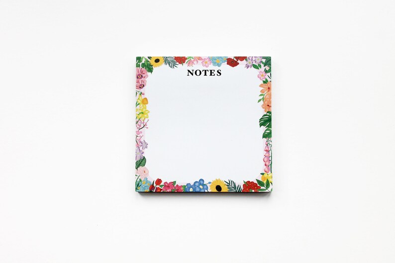 May include: A white notepad with a floral border. The border features a variety of colorful flowers, including pink, red, yellow, blue, and green. The notepad has the word "NOTES" printed in black at the top.