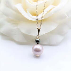 May include: A delicate gold chain necklace with a single large pink pearl and a smaller black pearl pendant.
