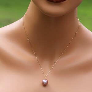 May include: A gold chain necklace with a single, large, round, iridescent pearl pendant. The pearl is a light pink color.