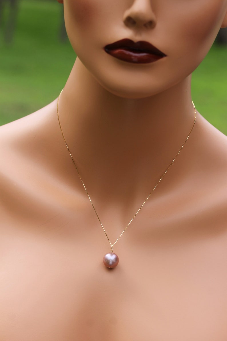 May include: A gold chain necklace with a single, large, round, iridescent pearl pendant. The pearl is a light pink color.