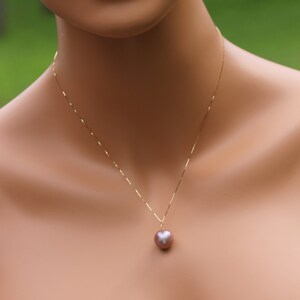 May include: A gold chain necklace with a single, large, round, iridescent pearl pendant. The pearl is a light pink color with a slight purple hue.