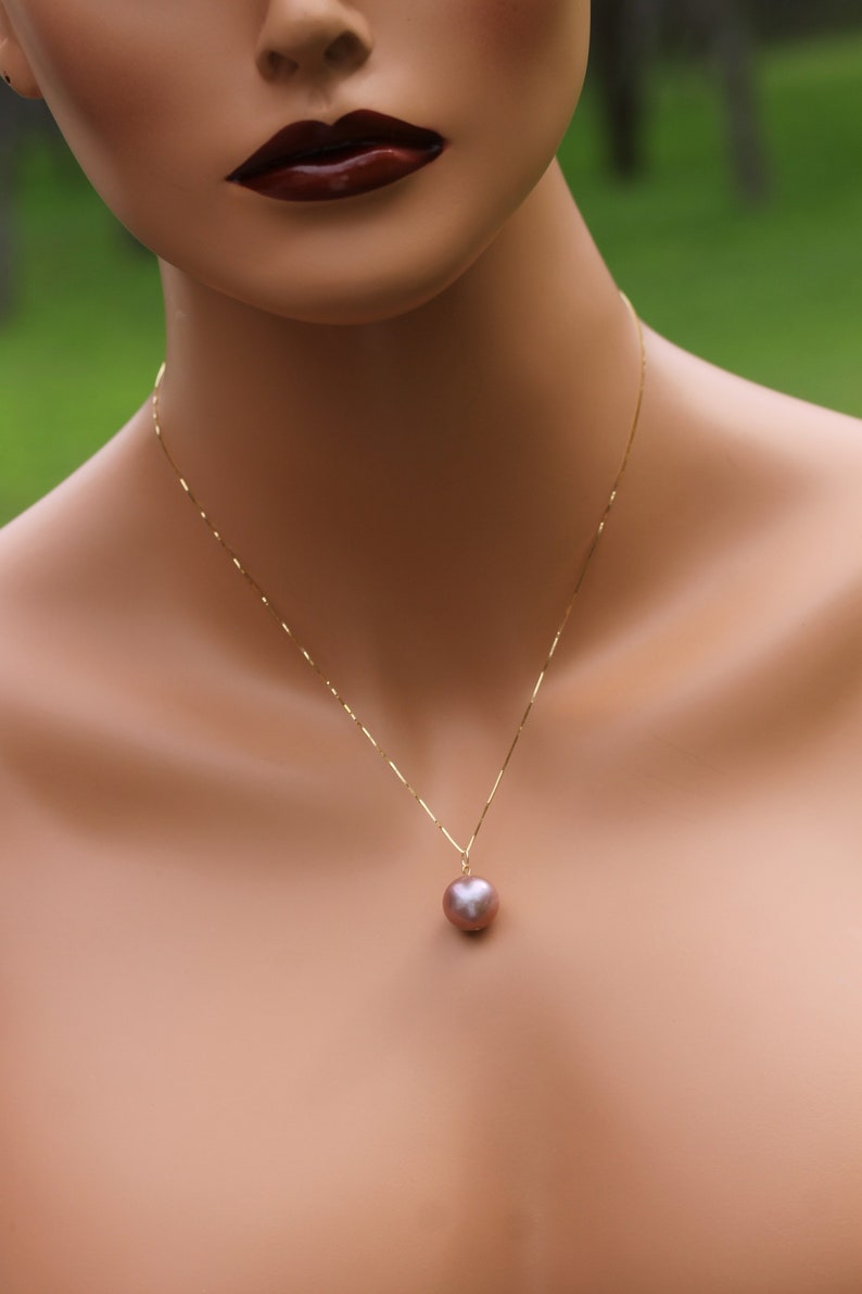 May include: A gold chain necklace with a single, large, round, iridescent pearl pendant. The pearl is a light pink color with a slight purple hue.