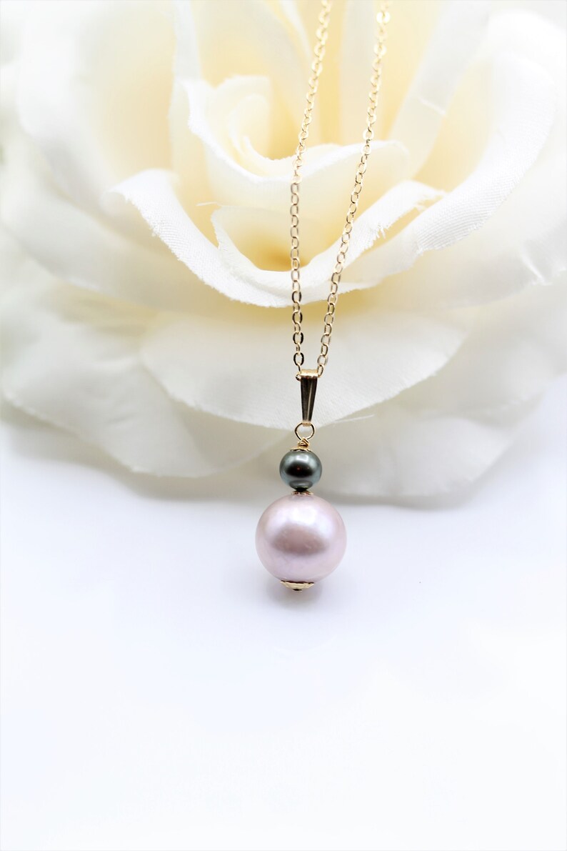 May include: A delicate gold chain necklace with a single large pink pearl and a smaller black pearl pendant.