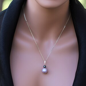 May include: A silver chain necklace with a single pearl pendant. The pearl is a light purple color and has a smaller black pearl accent.