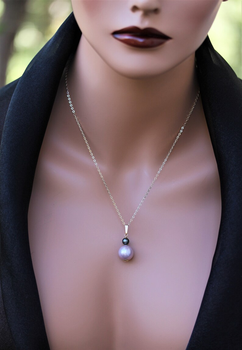 May include: A silver chain necklace with a single pearl pendant. The pearl is a light purple color and has a smaller black pearl accent.