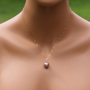 May include: A gold chain necklace with a single large, round, iridescent pearl pendant. The pearl is a light pink color.