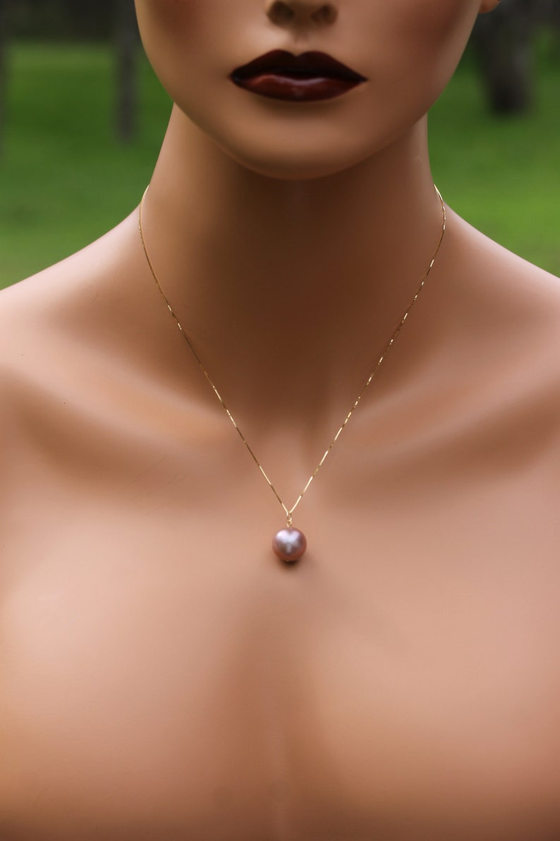 May include: A gold chain necklace with a single large, round, iridescent pearl pendant. The pearl is a light pink color.