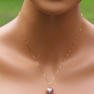 May include: A gold chain necklace with a single large, round, iridescent pearl pendant. The pearl is a light pink color.