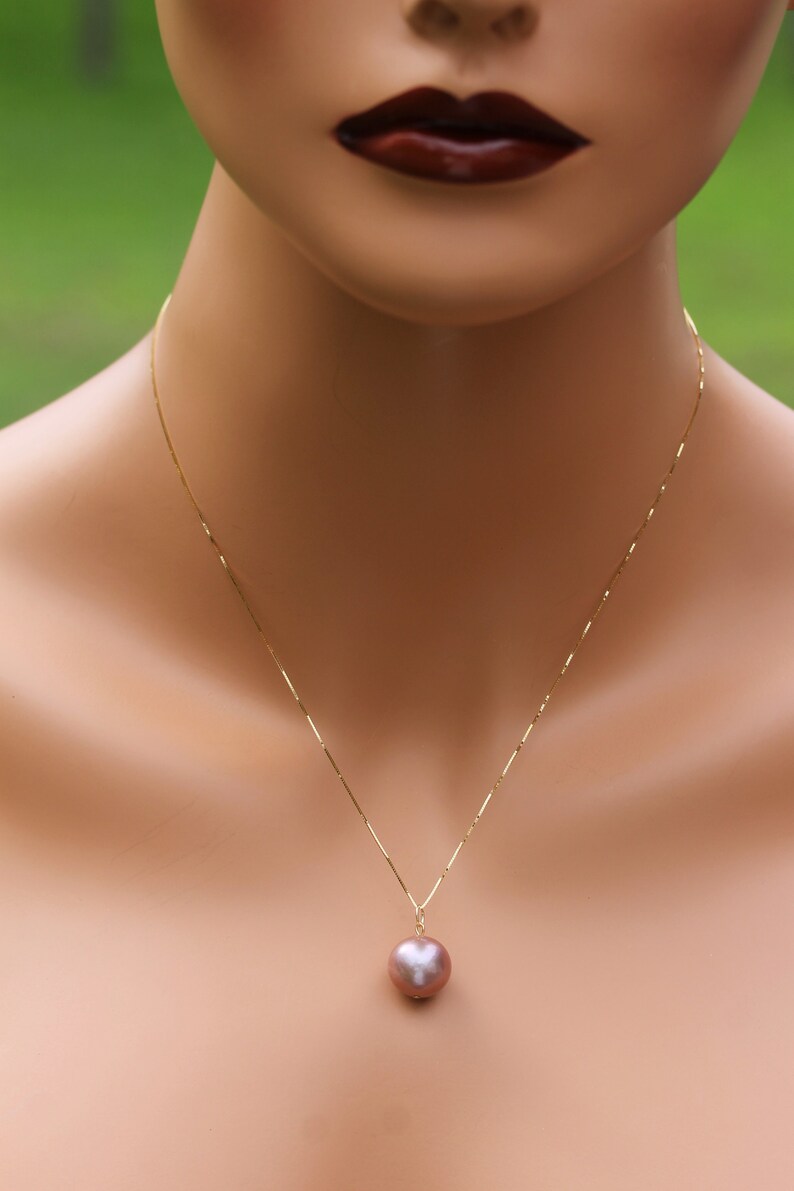 May include: A gold chain necklace with a single large, round, iridescent pearl pendant. The pearl is a light pink color.