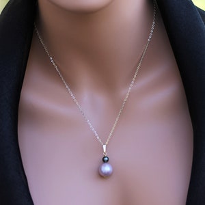 May include: A silver chain necklace with a pendant featuring a large, light purple pearl and a smaller, black pearl.