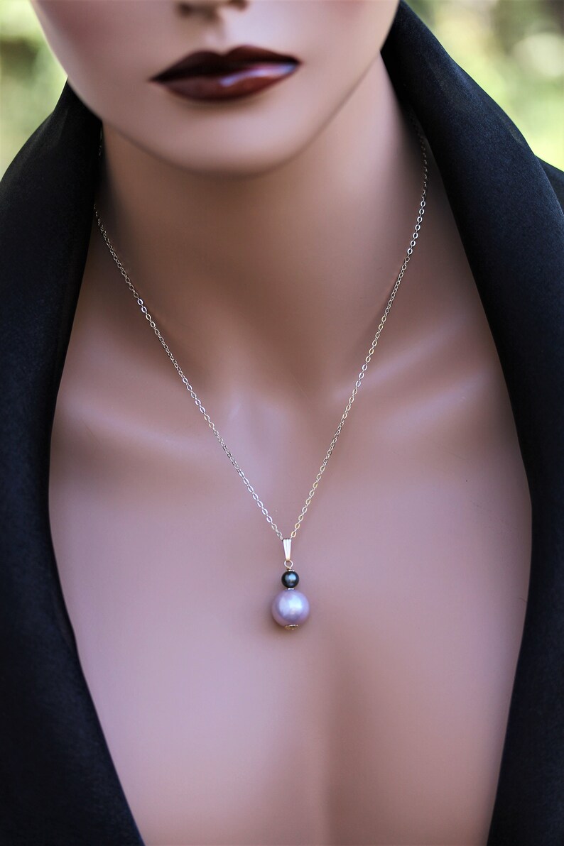 May include: A silver chain necklace with a pendant featuring a large, light purple pearl and a smaller, black pearl.