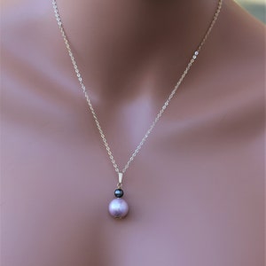 May include: A delicate gold chain necklace with a pendant featuring a single large, light pink pearl and a smaller, dark grey pearl.