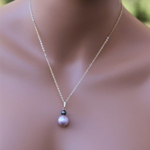 May include: A delicate gold chain necklace with a pendant featuring a large, light purple pearl and a smaller, black pearl.