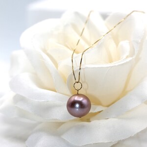 May include: A delicate gold chain necklace with a single, large, round, iridescent purple pearl pendant.