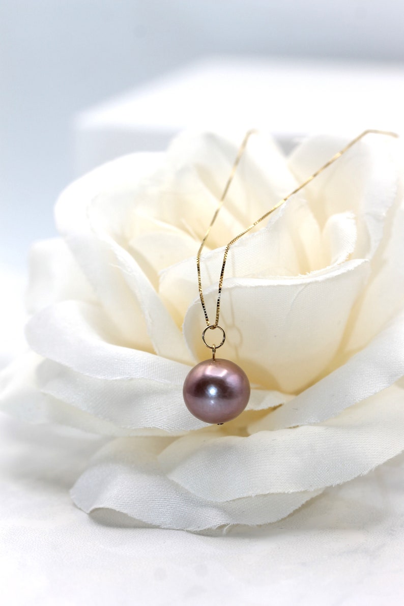 May include: A delicate gold chain necklace with a single, large, round, iridescent purple pearl pendant.