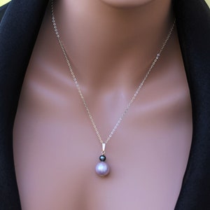 May include: A silver chain necklace with a pendant featuring a black and a lavender pearl.