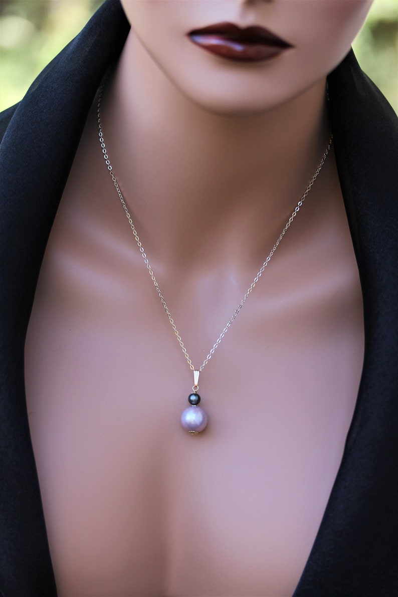 May include: A silver chain necklace with a pendant featuring a black and a lavender pearl.