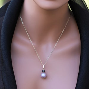 May include: A silver chain necklace with a pendant featuring a large, iridescent purple pearl and a smaller black pearl.