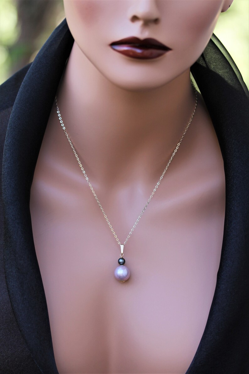 May include: A silver chain necklace with a pendant featuring a large, iridescent purple pearl and a smaller black pearl.