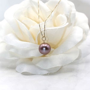 May include: A delicate gold chain necklace with a single, large, round, iridescent pearl pendant. The pearl is a soft, muted pink color.