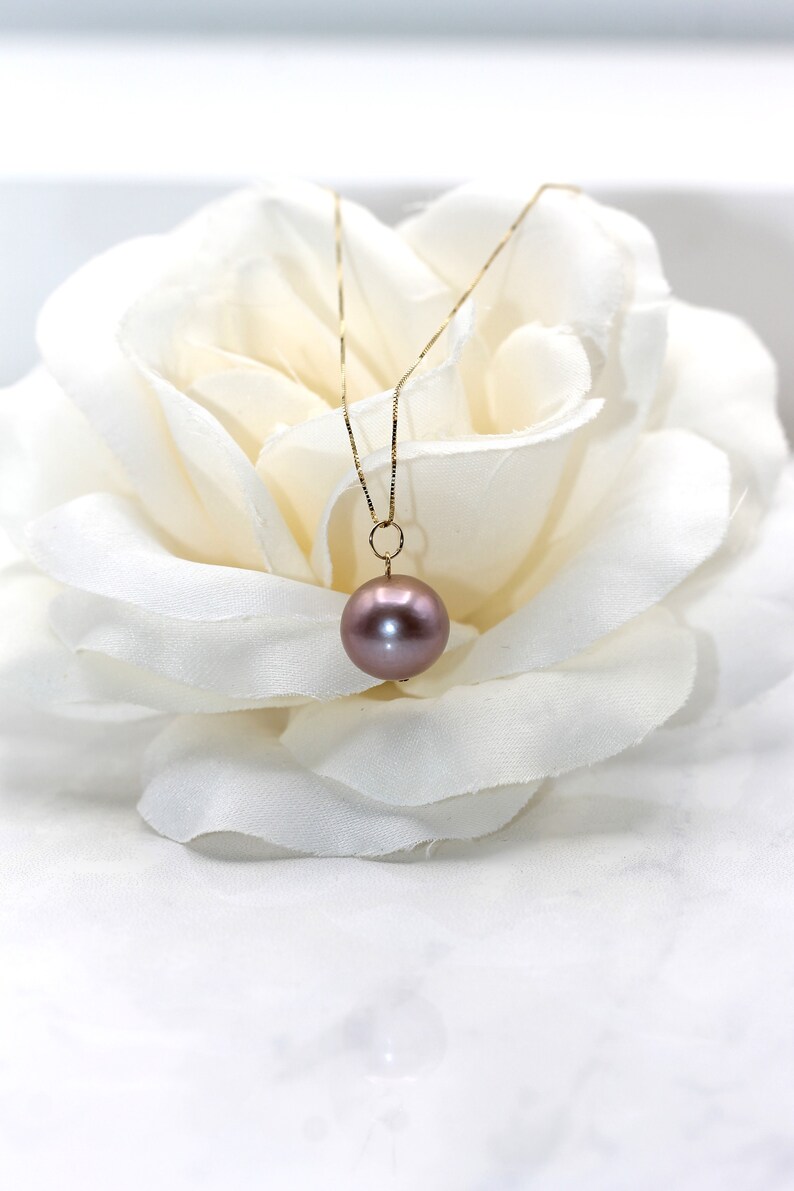 May include: A delicate gold chain necklace with a single, large, round, iridescent pearl pendant. The pearl is a soft, muted pink color.