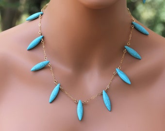 May include: A gold chain necklace with turquoise teardrop-shaped pendants. The necklace is paired with matching turquoise teardrop earrings.