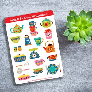 May include: A sticker sheet featuring assorted vintage kitchenware illustrations. The designs include teapots, cups, bowls, a grater, a scale, and a jam jar. The sticker sheet has a red border and the text "Assorted Vintage Kitchenware". A succulent plant is next to the sticker sheet.