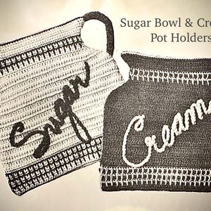 May include: Crocheted pot holders in the shape of a sugar bowl and creamer. The sugar bowl holder is white with black lettering and trim. The creamer holder is dark gray with white lettering and trim. The text "Sugar Bowl & Creamer Pot Holders" is at the top.