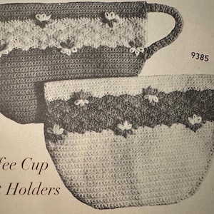 May include: Two crocheted coffee cup pot holders. The pot holders are in the shape of a coffee cup with a handle. The pot holders are white, dark grey, and light grey with flower accents. The text "Coffee Cup Pot Holders" is at the bottom of the image.