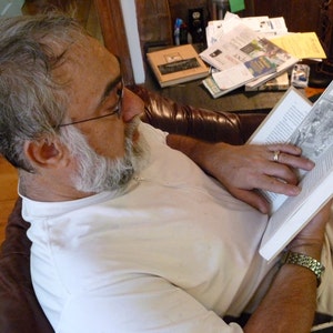 May include: A man is sitting in a chair and reading a book. The book has a bookmark that says "In My Book".